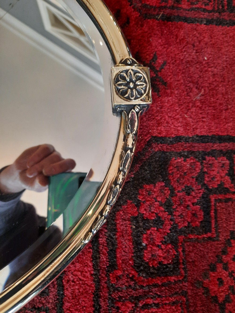 A late 19th-century oval mirror featuring a polished brass frame with decorative scrolled cresting and rosette side accents. View III