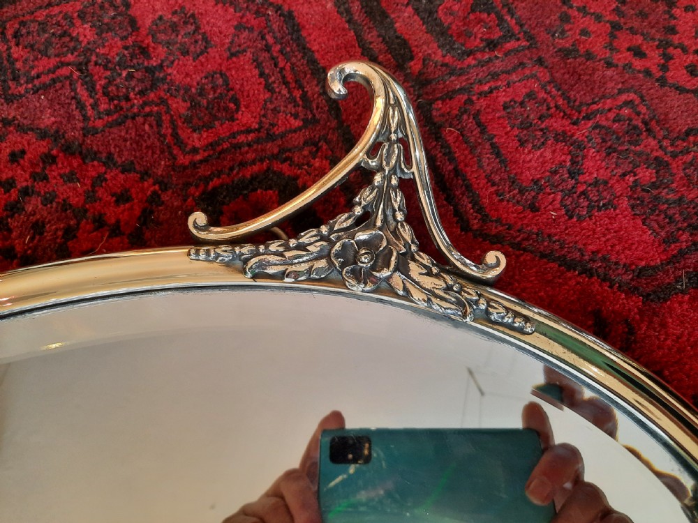 A late 19th-century oval mirror featuring a polished brass frame with decorative scrolled cresting and rosette side accents. View IV