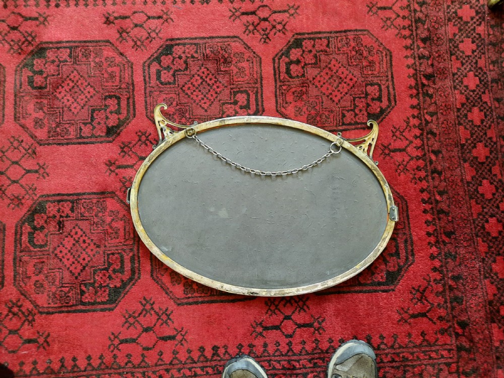 A late 19th-century oval mirror featuring a polished brass frame with decorative scrolled cresting and rosette side accents. View V