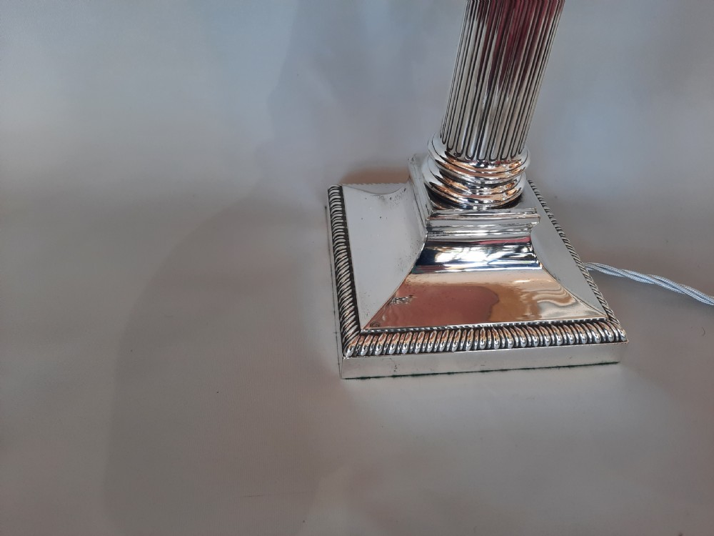 A silver-plated table lamp styled as a fluted Corinthian column with a stepped square base, topped with a scalloped pink fabric shade adorned with long beaded fringe. View III