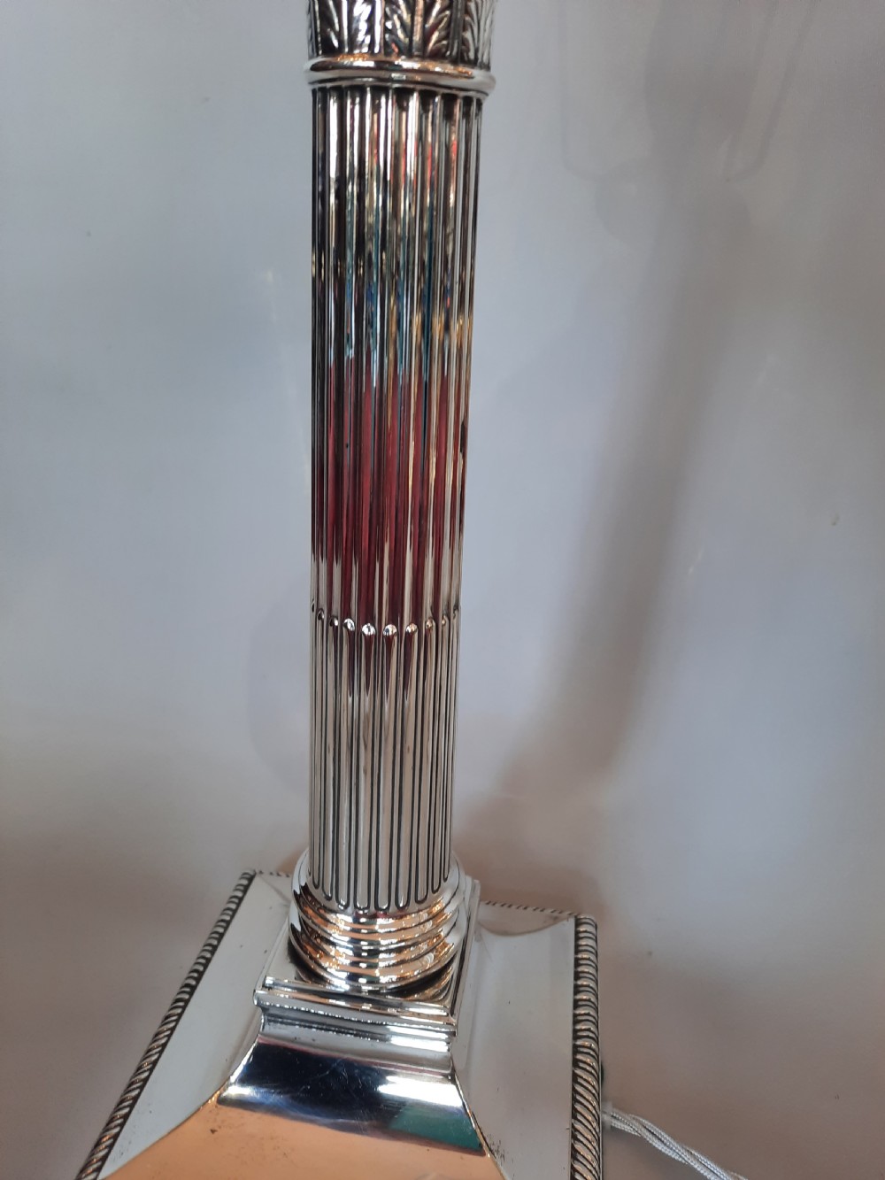 A silver-plated table lamp styled as a fluted Corinthian column with a stepped square base, topped with a scalloped pink fabric shade adorned with long beaded fringe. View IV