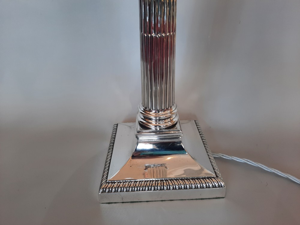 A silver-plated table lamp styled as a fluted Corinthian column with a stepped square base, topped with a scalloped pink fabric shade adorned with long beaded fringe. View VI