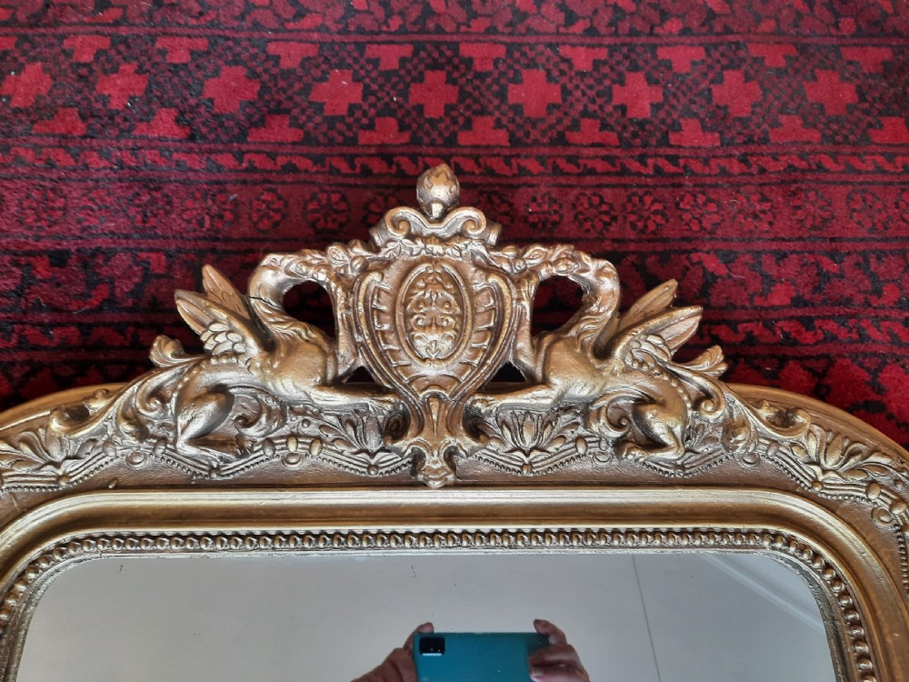 A 19th-century French gilded wall mirror featuring an arched frame topped with a carved crest of winged dragons and a central shield. View II