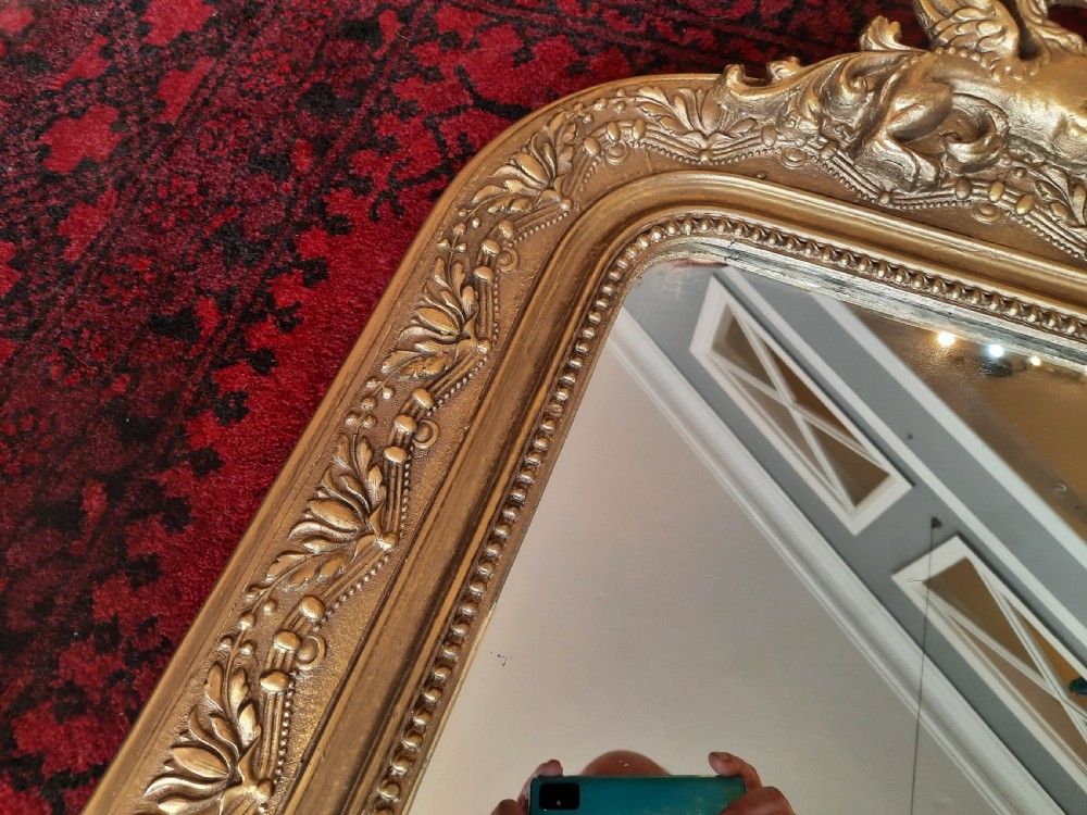 A 19th-century French gilded wall mirror featuring an arched frame topped with a carved crest of winged dragons and a central shield. View III