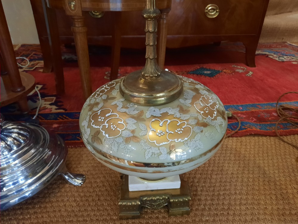 A pair of late Victorian table lamps featuring ornate gilt brass stems, painted glass baluster bases, and cream silk shades with fringe tassels. View IV