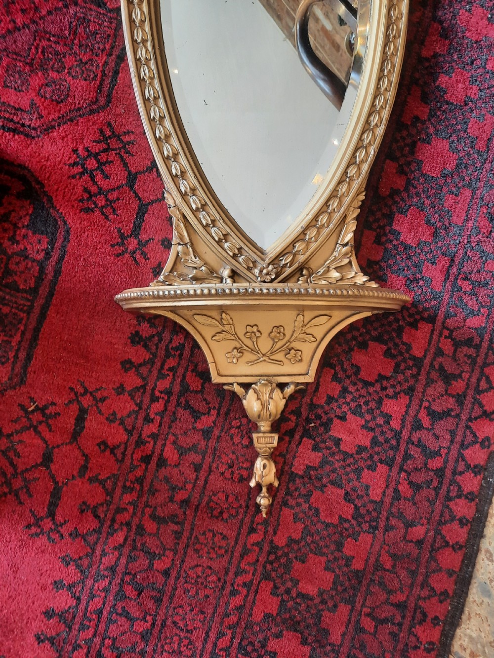 A Victorian Neoclassical giltwood wall mirror featuring a shield-shaped frame, scroll carved cresting, an integrated lower shelf, and a pendant drop finial. View II