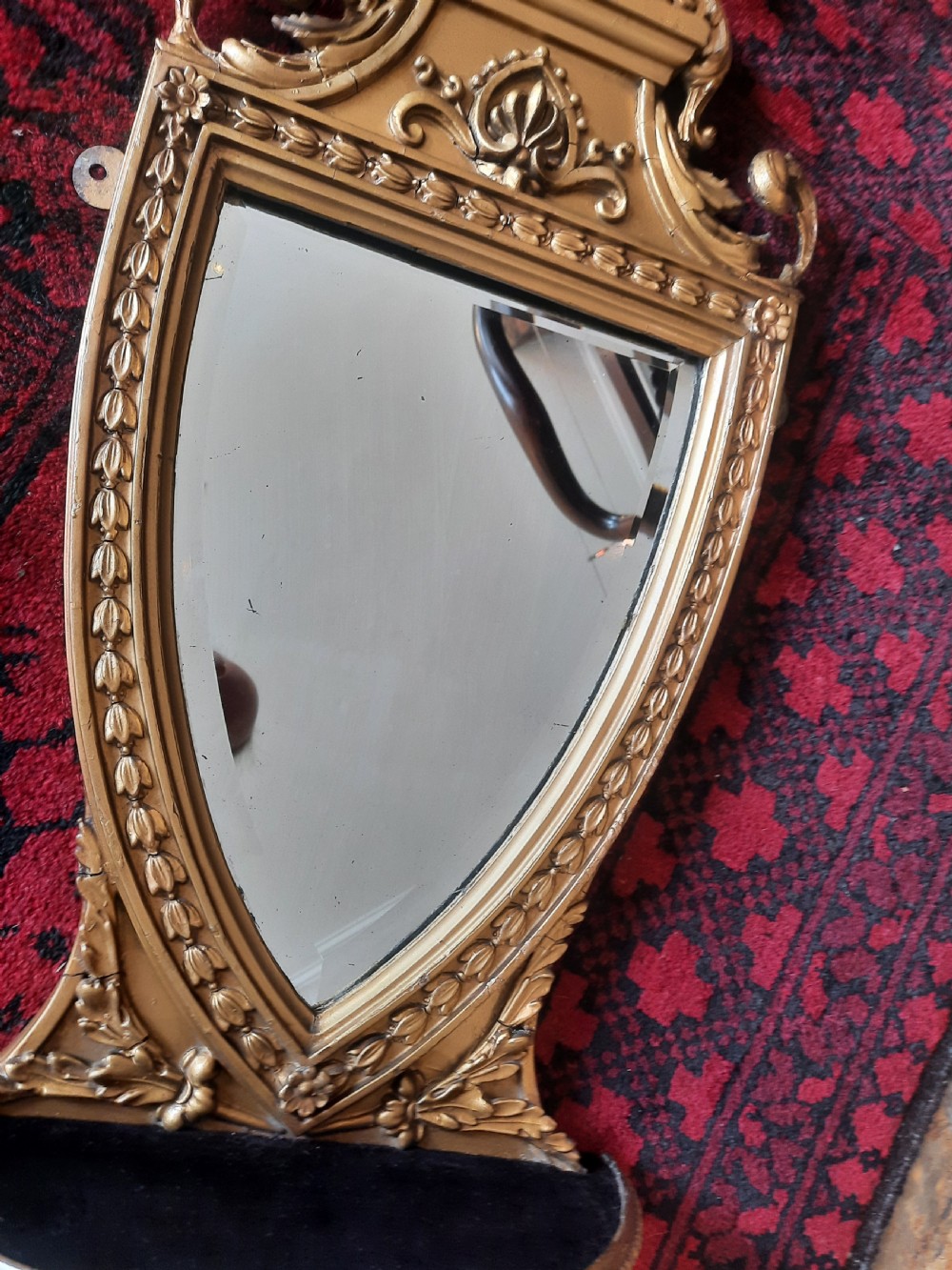 A Victorian Neoclassical giltwood wall mirror featuring a shield-shaped frame, scroll carved cresting, an integrated lower shelf, and a pendant drop finial. View IV