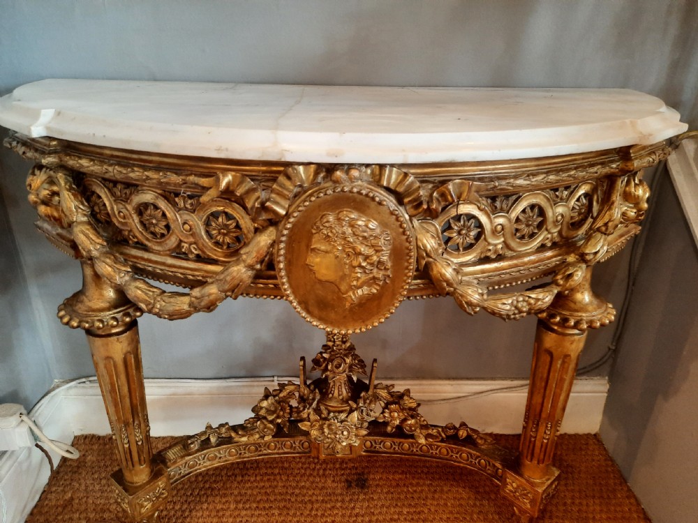 An early 19th-century semicircular giltwood console table featuring a white marble top, carved classical medallion, decorative swags, and fluted legs. View III