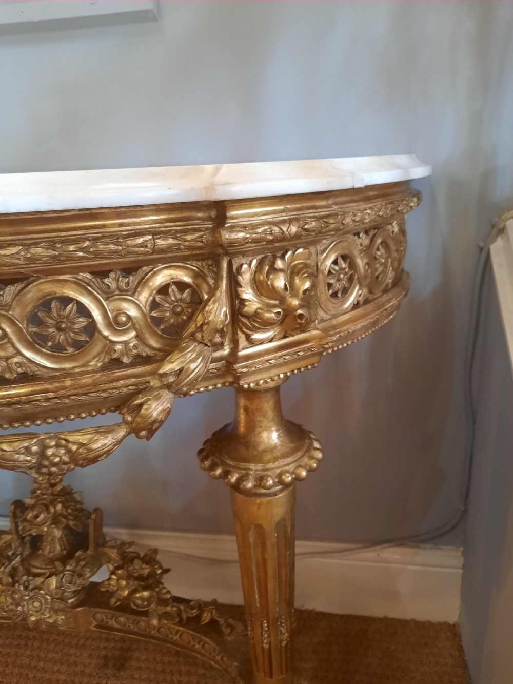 An early 19th-century semicircular giltwood console table featuring a white marble top, carved classical medallion, decorative swags, and fluted legs. View VI