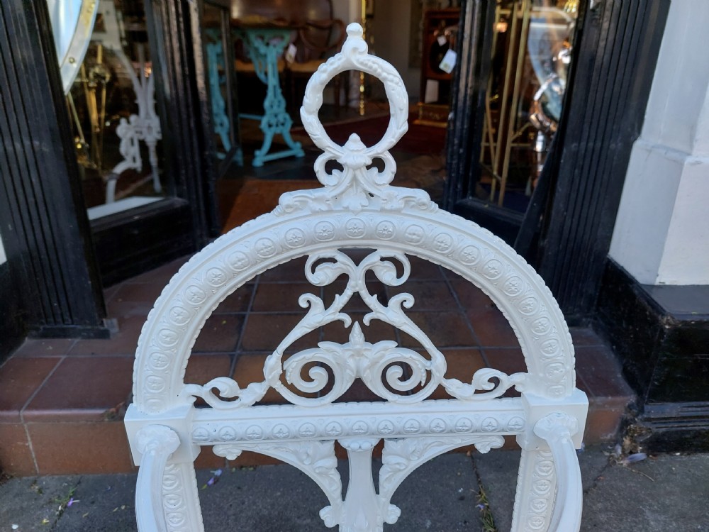 A white painted cast iron Victorian stick stand featuring detailed scrollwork, an arched backplate frame with a top ring, a central pedestal, and a curved drip tray base. View IV