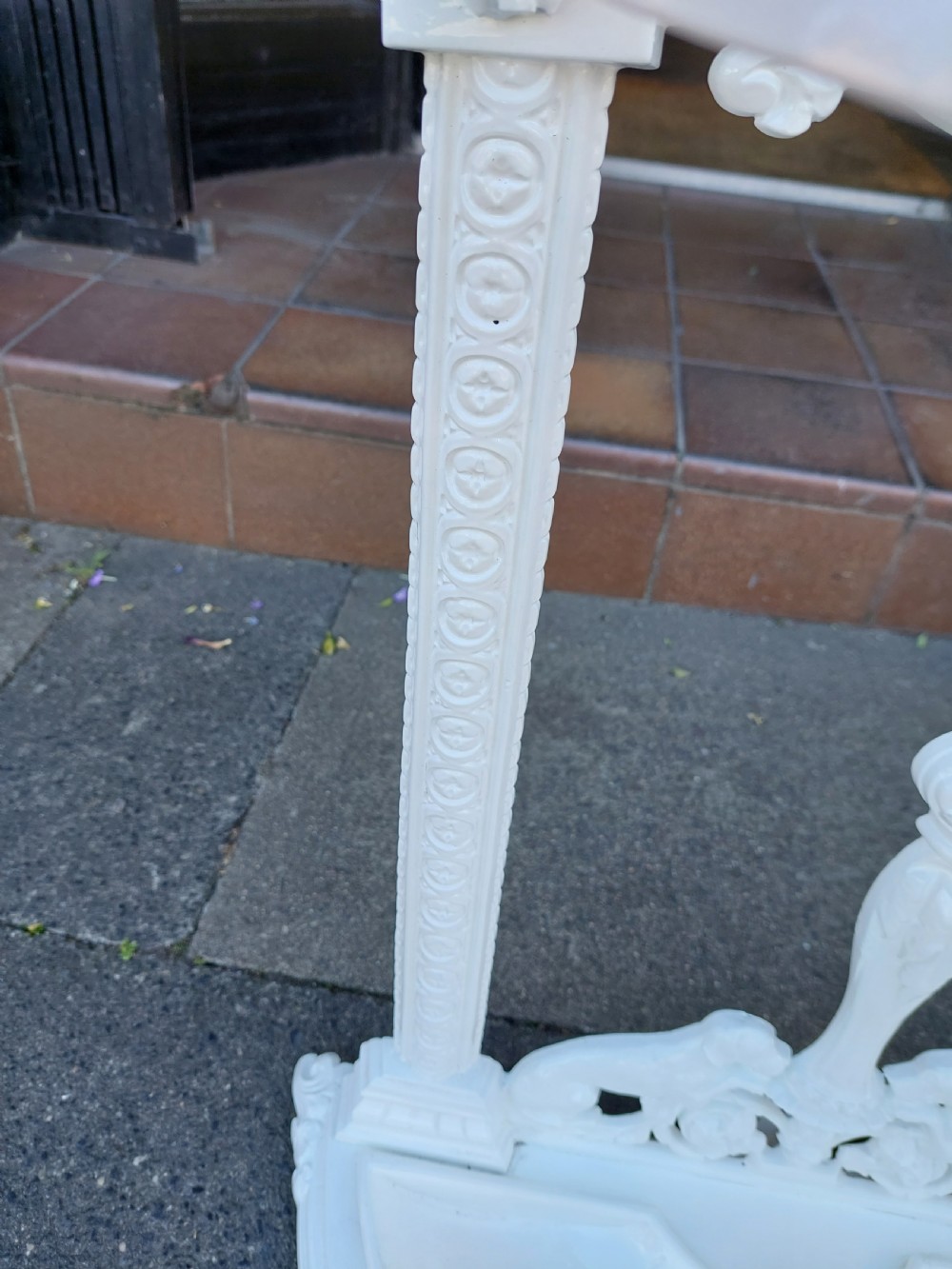 A white painted cast iron Victorian stick stand featuring detailed scrollwork, an arched backplate frame with a top ring, a central pedestal, and a curved drip tray base. View V
