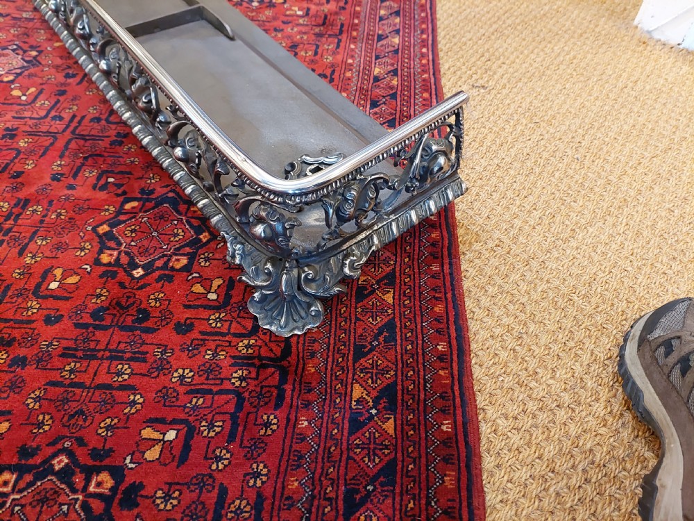 A 19th-century polished steel and iron fireplace fender featuring detailed openwork scroll motifs and shaped corner feet. View II