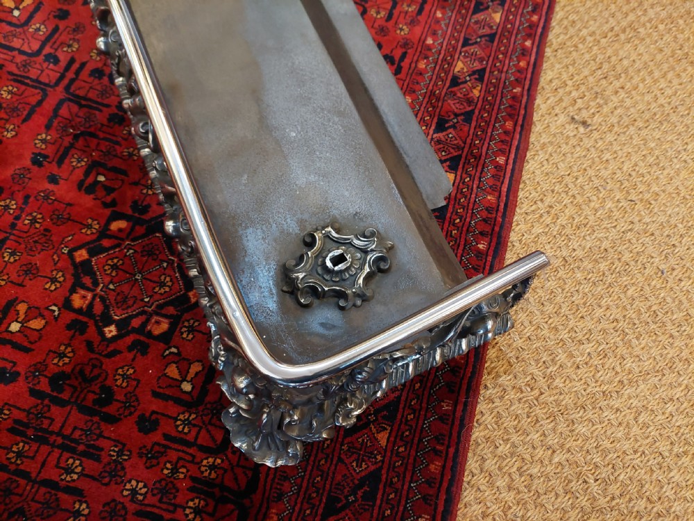 A 19th-century polished steel and iron fireplace fender featuring detailed openwork scroll motifs and shaped corner feet. View III