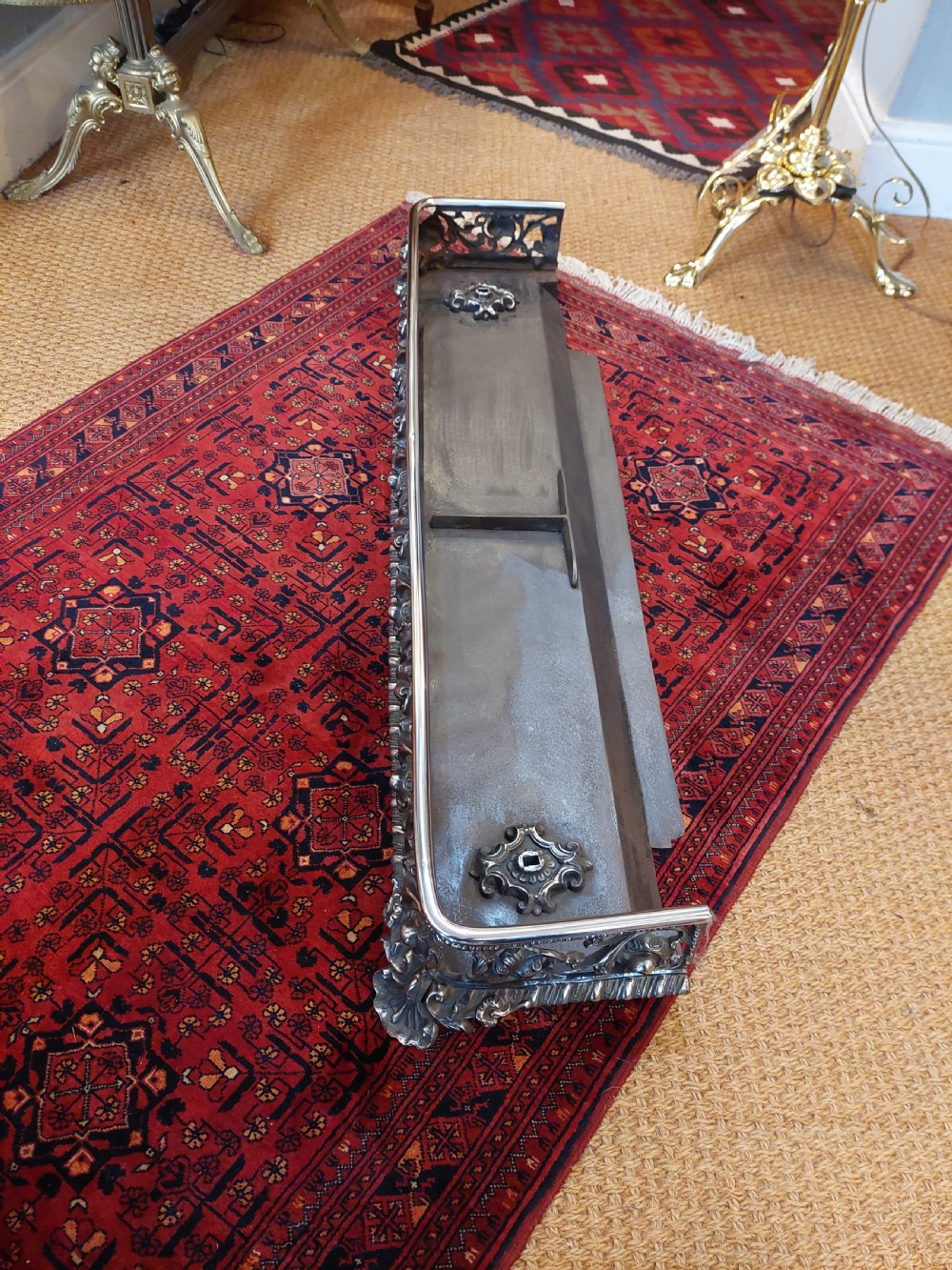 A 19th-century polished steel and iron fireplace fender featuring detailed openwork scroll motifs and shaped corner feet. View IV