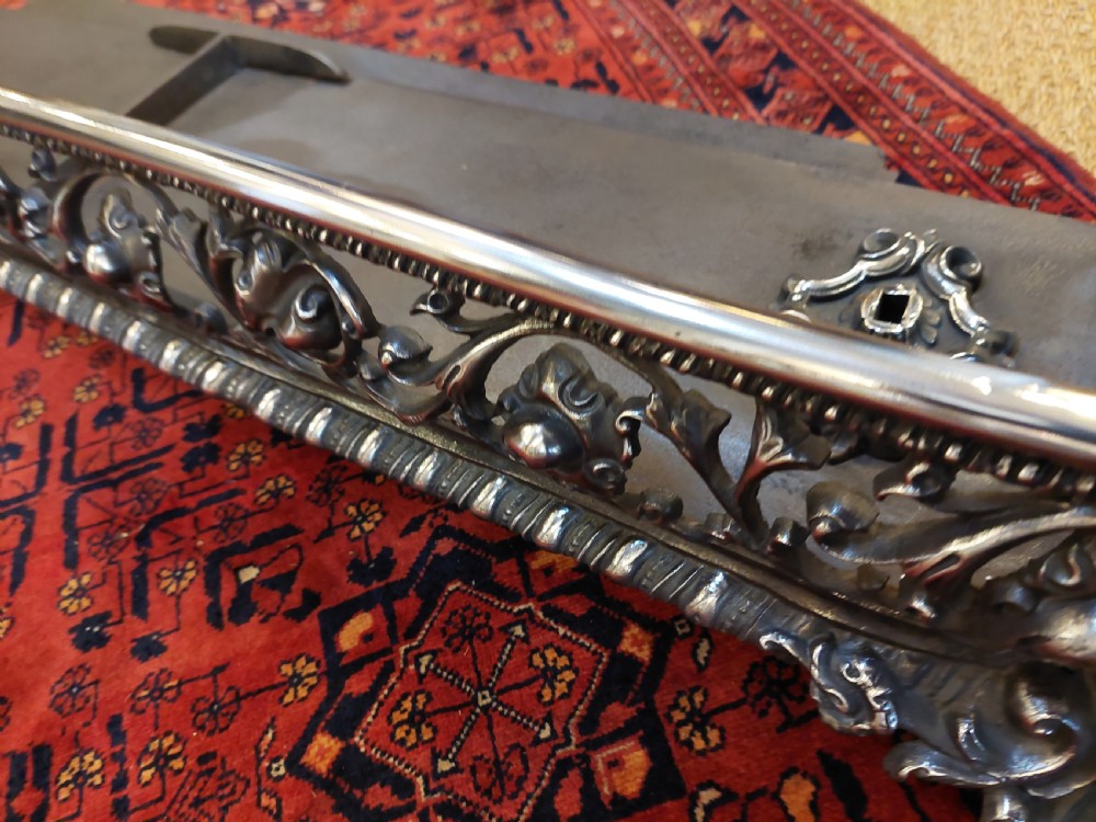 A 19th-century polished steel and iron fireplace fender featuring detailed openwork scroll motifs and shaped corner feet. View VI