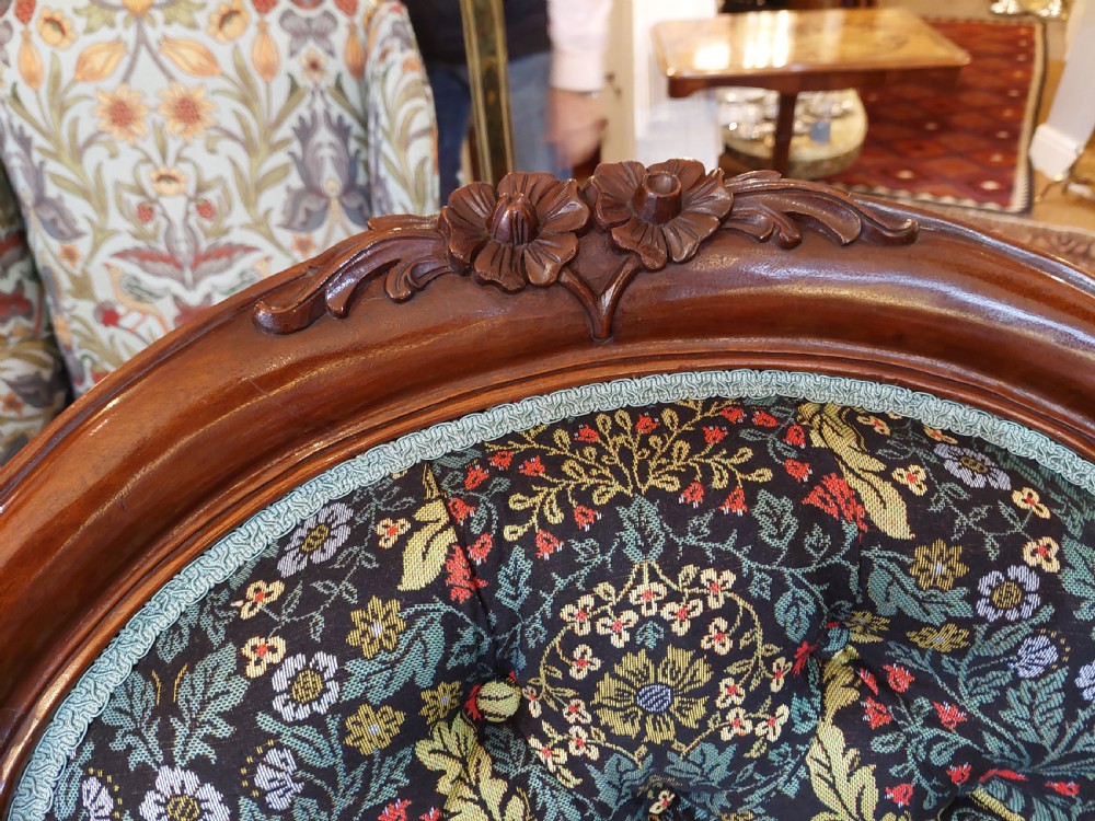 Victorian mahogany scroll frame armchair upholstered in a dark botanical floral fabric with a button-backed cushion and carved cabriole legs on castors. View V