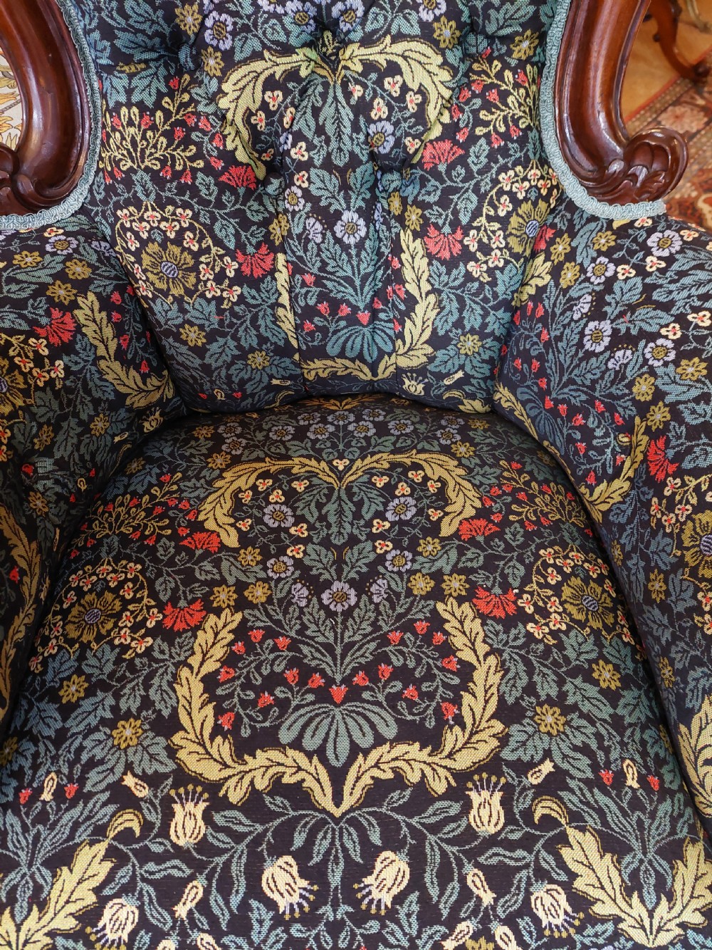 Victorian mahogany scroll frame armchair upholstered in a dark botanical floral fabric with a button-backed cushion and carved cabriole legs on castors. View X