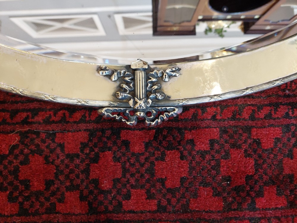 An early 20th-century oval mirror featuring a hand-hammered brass frame with decorative mounts at four cardinal points and a bevelled central glass plate. View II