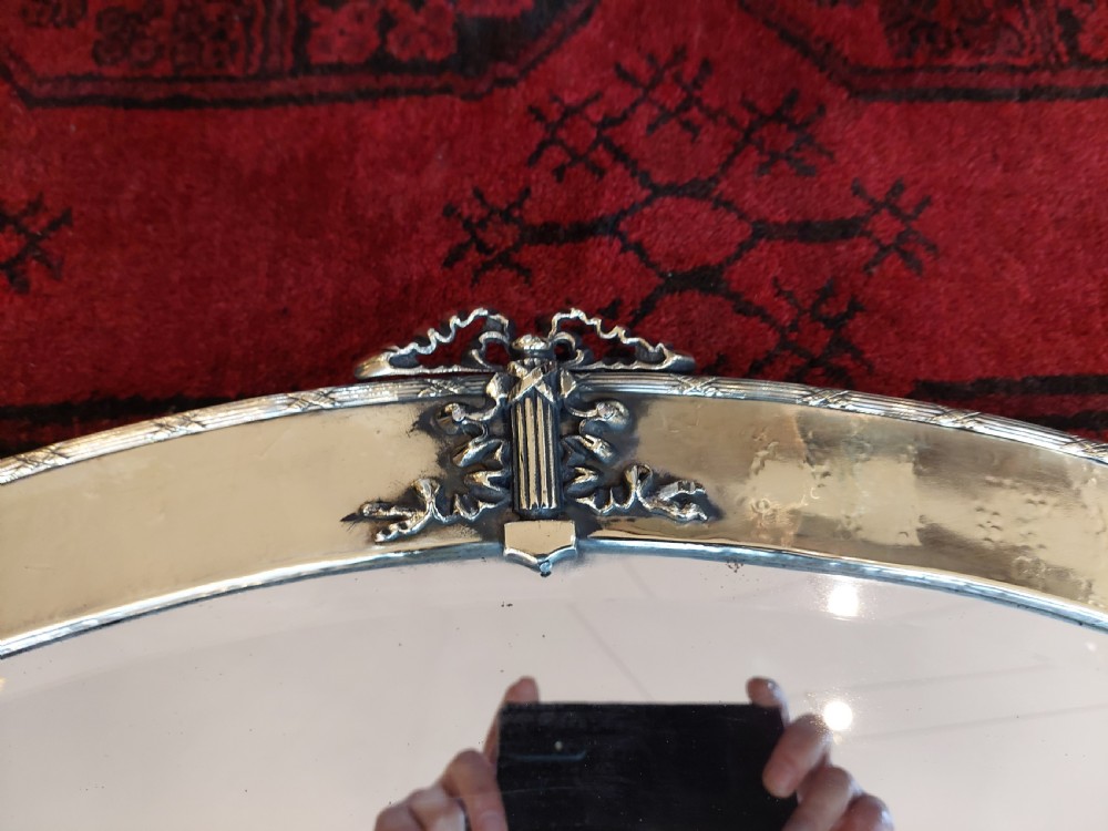An early 20th-century oval mirror featuring a hand-hammered brass frame with decorative mounts at four cardinal points and a bevelled central glass plate. View III