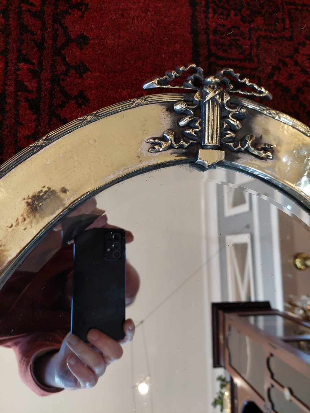 An early 20th-century oval mirror featuring a hand-hammered brass frame with decorative mounts at four cardinal points and a bevelled central glass plate. View IV