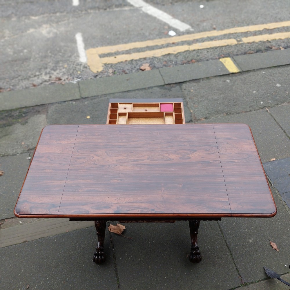 A Regency rosewood work table featuring drop leaves, a single frieze drawer, a red patterned fabric sewing well below, turned pedestal supports, and carved claw feet. View IX