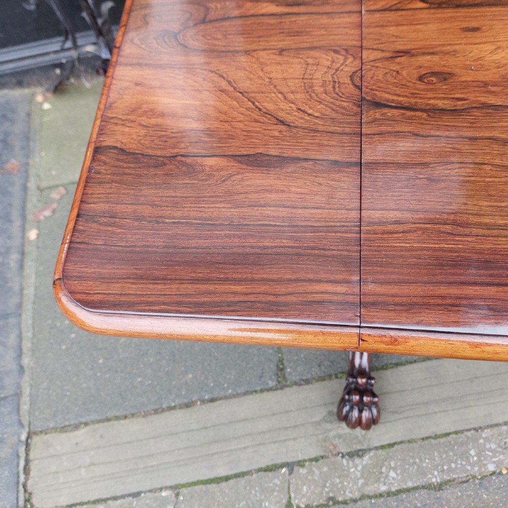 A Regency rosewood work table featuring drop leaves, a single frieze drawer, a red patterned fabric sewing well below, turned pedestal supports, and carved claw feet. View X