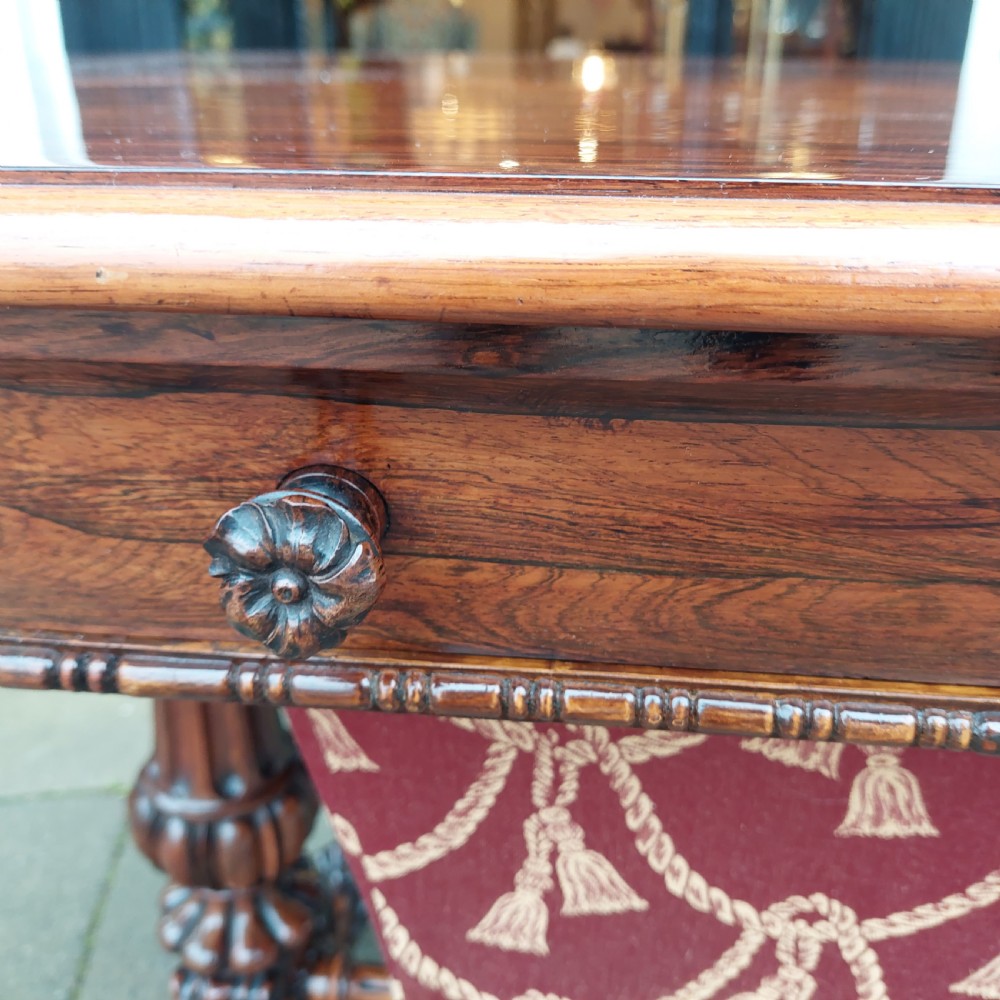 A Regency rosewood work table featuring drop leaves, a single frieze drawer, a red patterned fabric sewing well below, turned pedestal supports, and carved claw feet. View XI