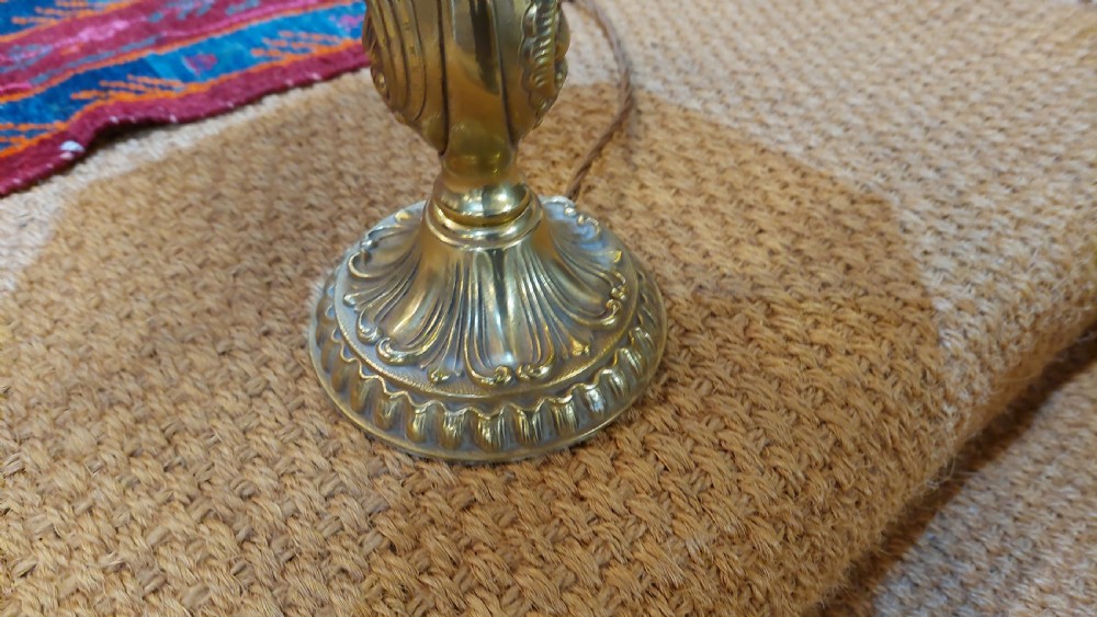 An early 20th-century table lamp featuring an embossed pressed brass stem and a dome-shaped red fabric shade trimmed with cream fringe and tassels. View II
