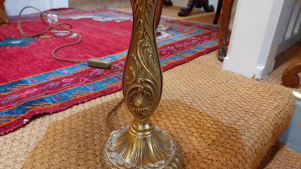 An early 20th-century table lamp featuring an embossed pressed brass stem and a dome-shaped red fabric shade trimmed with cream fringe and tassels. View III
