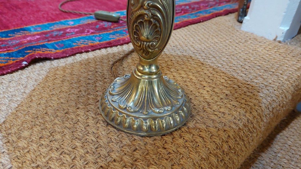 An early 20th-century table lamp featuring an embossed pressed brass stem and a dome-shaped red fabric shade trimmed with cream fringe and tassels. View IV