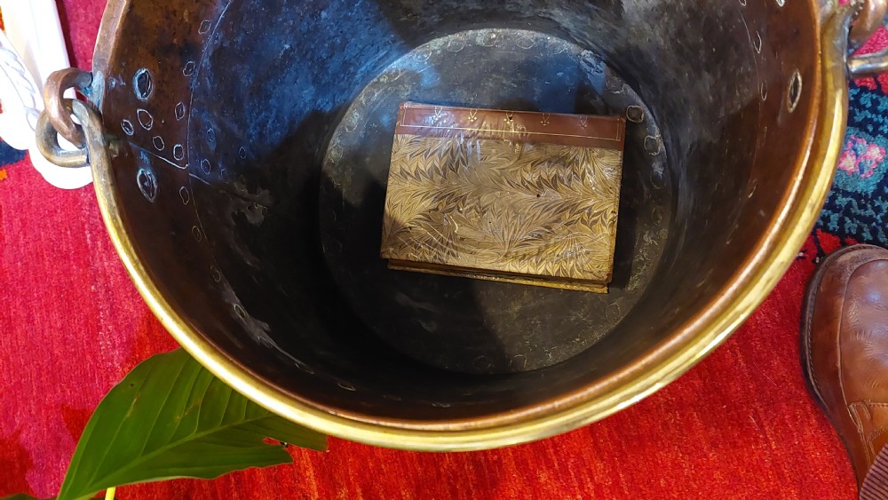 A circular Victorian copper log bucket featuring visible rivet construction along the seams and a brass swing handle. View V