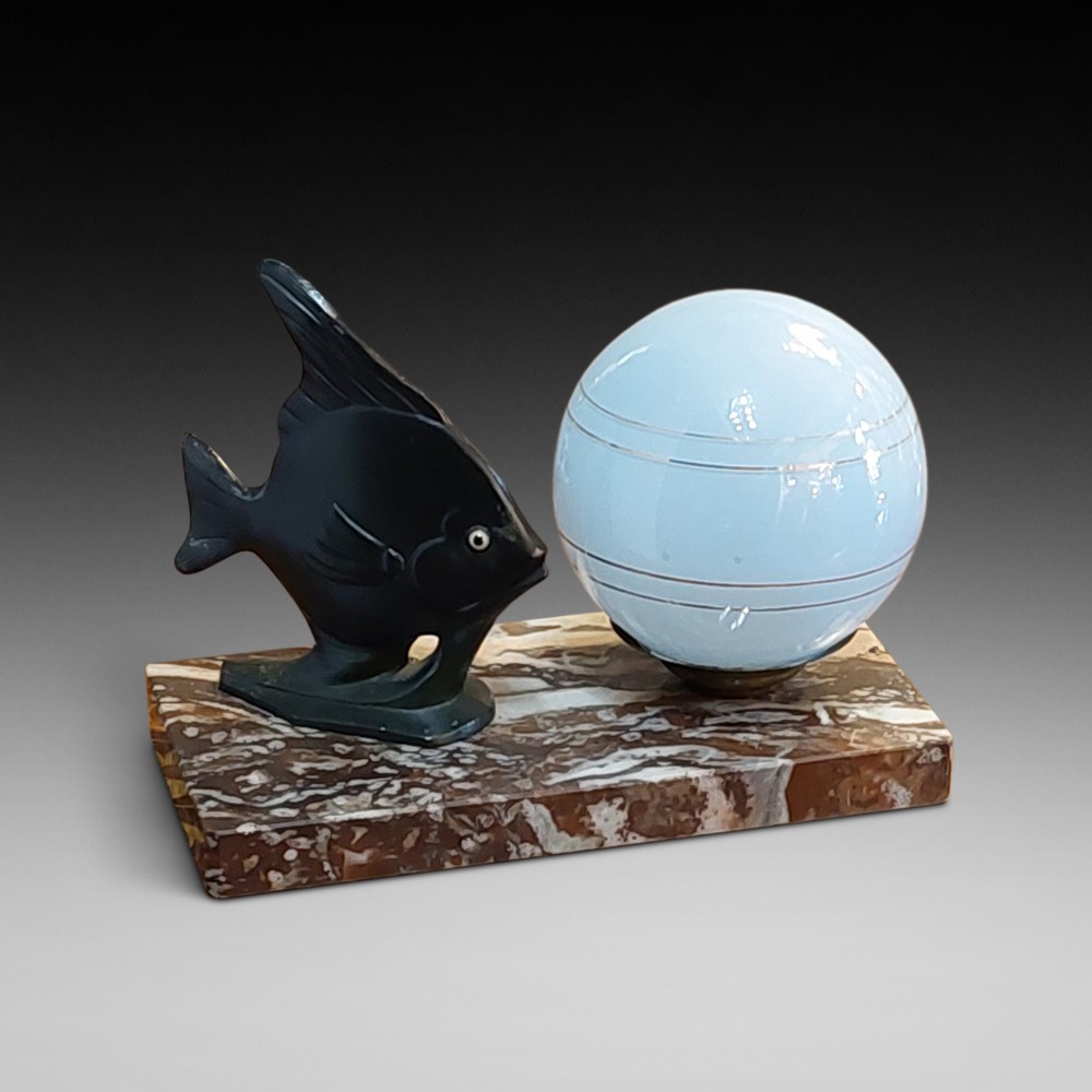 An Art Deco table lamp featuring a black sculptural fish figure beside a spherical glass shade on a rectangular marbled base.