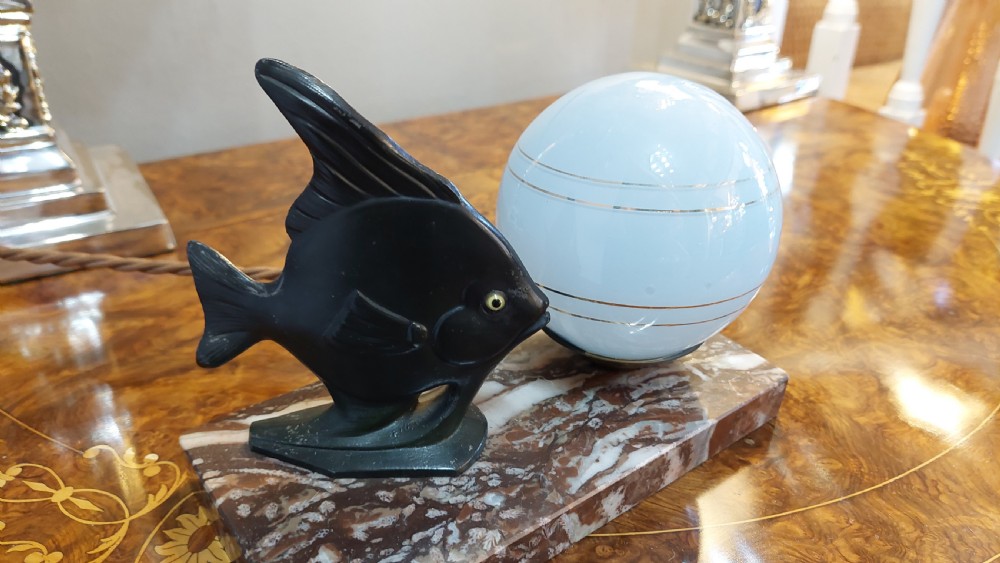 An Art Deco table lamp featuring a black sculptural fish figure beside a spherical glass shade on a rectangular marbled base. View II