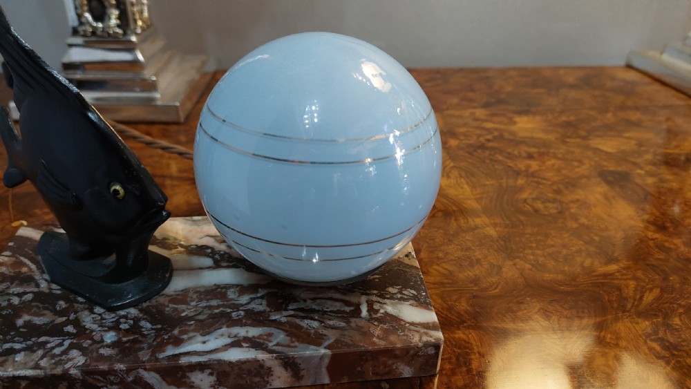 An Art Deco table lamp featuring a black sculptural fish figure beside a spherical glass shade on a rectangular marbled base. View III