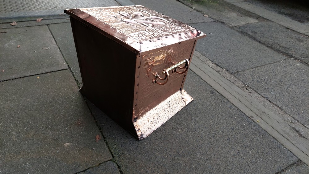 A square hand-hammered copper coal box featuring embossed stylised botanical motifs, riveted metal borders, side handles, and a flared base. View IV