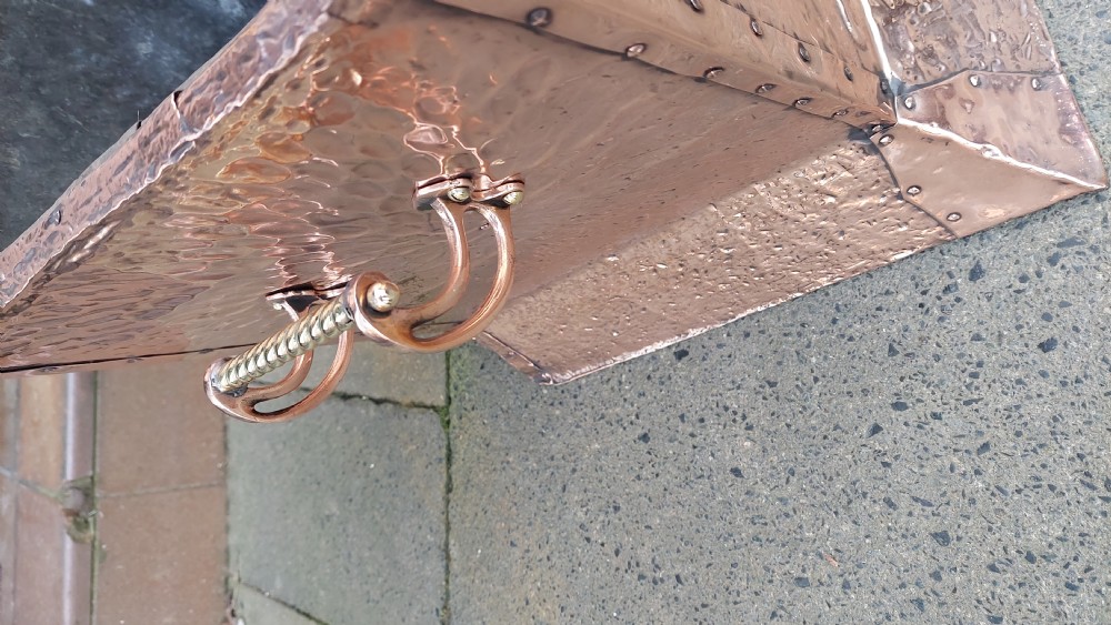 A square hand-hammered copper coal box featuring embossed stylised botanical motifs, riveted metal borders, side handles, and a flared base. View VII
