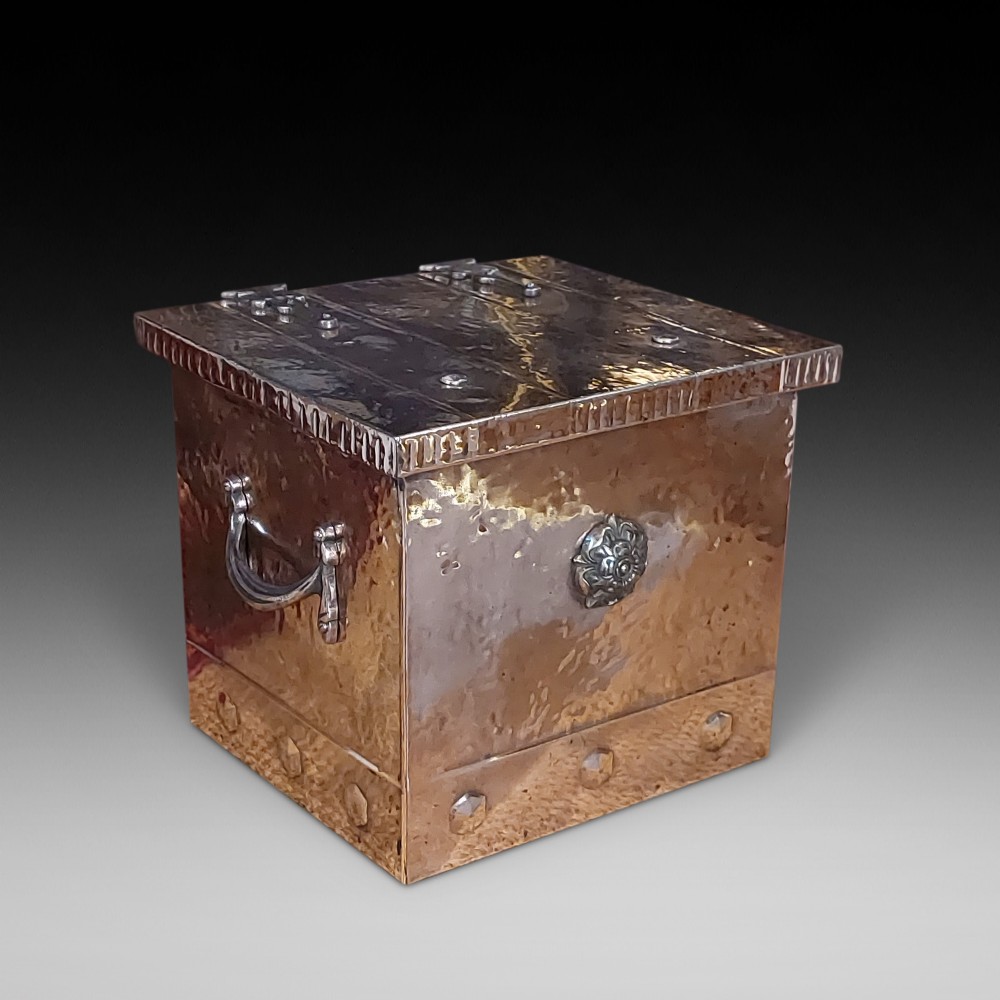 A late 19th-century square copper-plated coal box featuring a hammered finish, hinged lid, drop side handles, and decorative metal studs along the base.