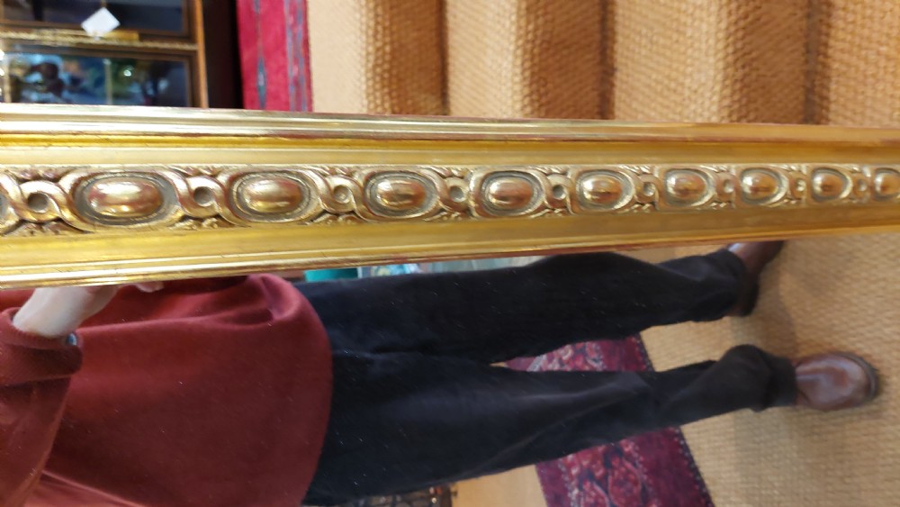 A large Victorian giltwood mirror featuring an arched upper frame, detailed bead moulding, and carved scroll feet at the base. View V