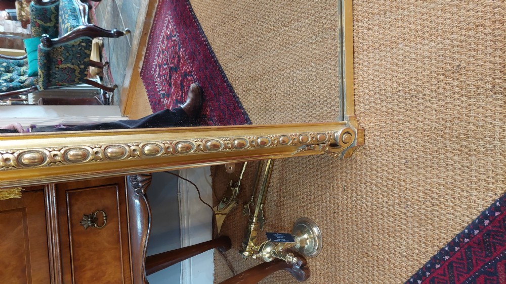 A large Victorian giltwood mirror featuring an arched upper frame, detailed bead moulding, and carved scroll feet at the base. View VIII