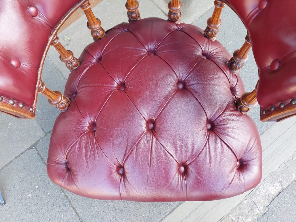 A Victorian mahogany captains desk chair featuring deep-buttoned burgundy leather upholstery, brass stud trim, turned spindles, and carved legs on brass castors. View V