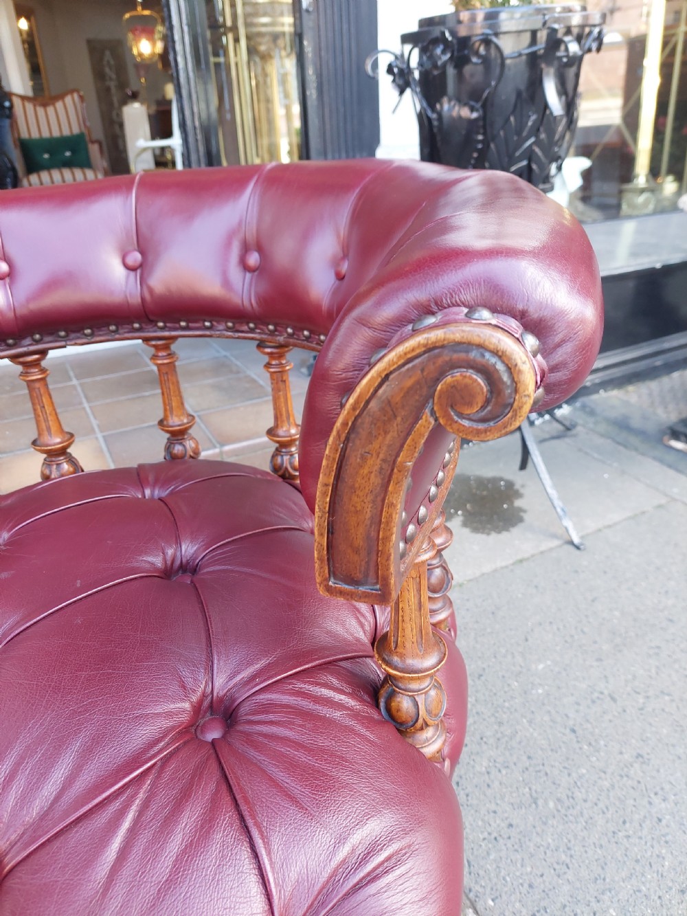 A Victorian mahogany captains desk chair featuring deep-buttoned burgundy leather upholstery, brass stud trim, turned spindles, and carved legs on brass castors. View VI