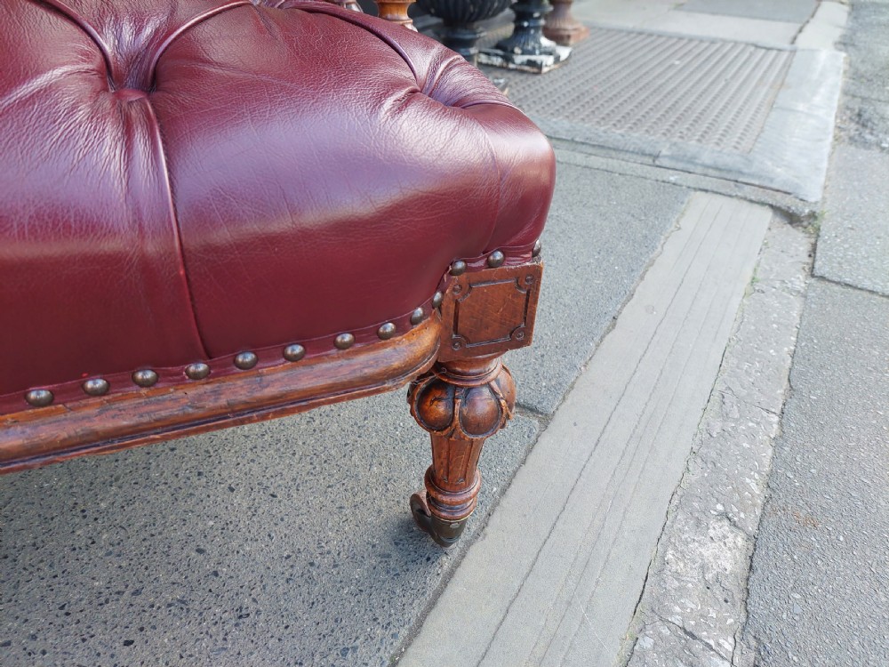 A Victorian mahogany captains desk chair featuring deep-buttoned burgundy leather upholstery, brass stud trim, turned spindles, and carved legs on brass castors. View VII