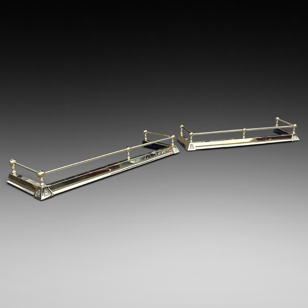 A pair of polished brass adjustable fireplace fenders featuring turned ball finials and telescopic rails.