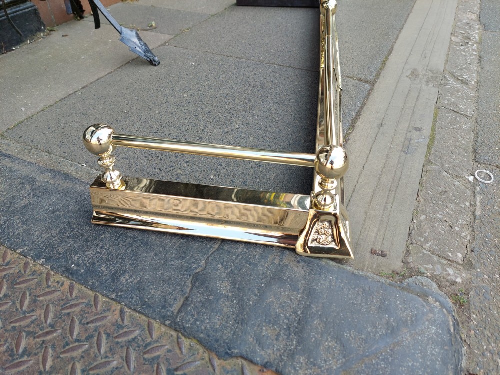 A pair of polished brass adjustable fireplace fenders featuring turned ball finials and telescopic rails. View V