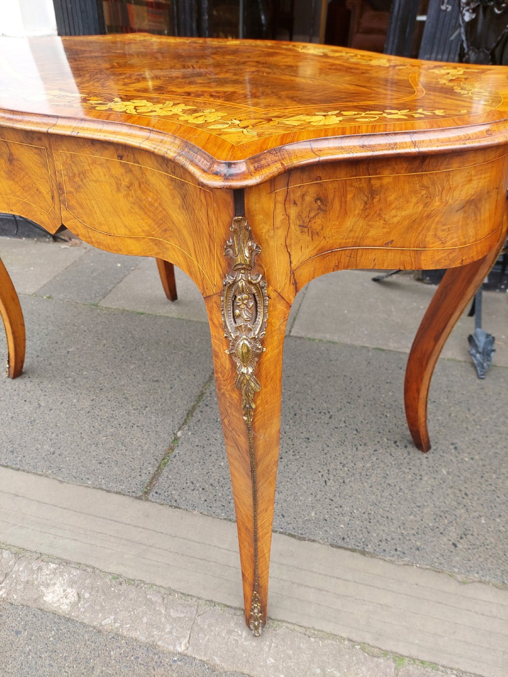 A 19th-century burr walnut bureau plat with a serpentine top featuring floral marquetry, gilt-bronze mounts, and cabriole legs. View II