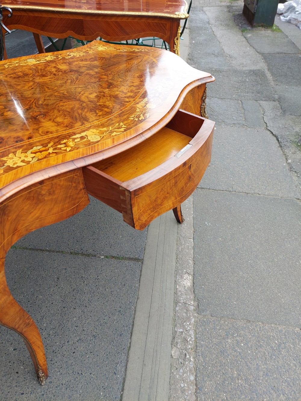 A 19th-century burr walnut bureau plat with a serpentine top featuring floral marquetry, gilt-bronze mounts, and cabriole legs. View V