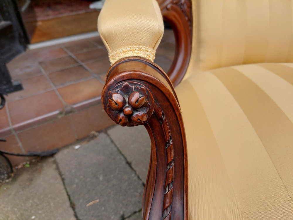 A low Victorian armchair crafted from carved dark walnut with cream striped upholstery and turned legs with brass casters. View IV