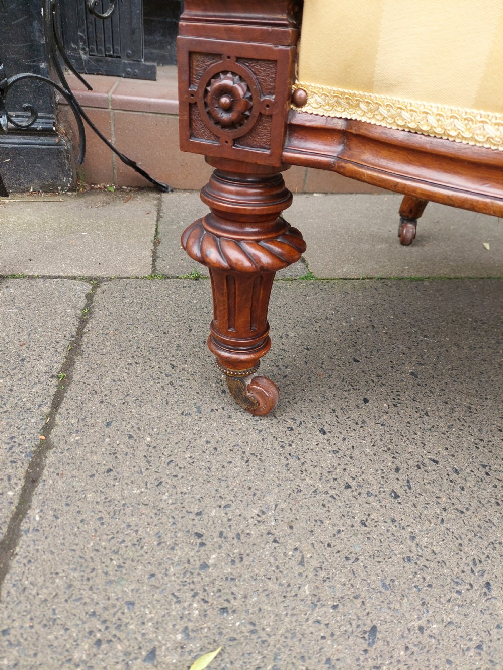 A low Victorian armchair crafted from carved dark walnut with cream striped upholstery and turned legs with brass casters. View V