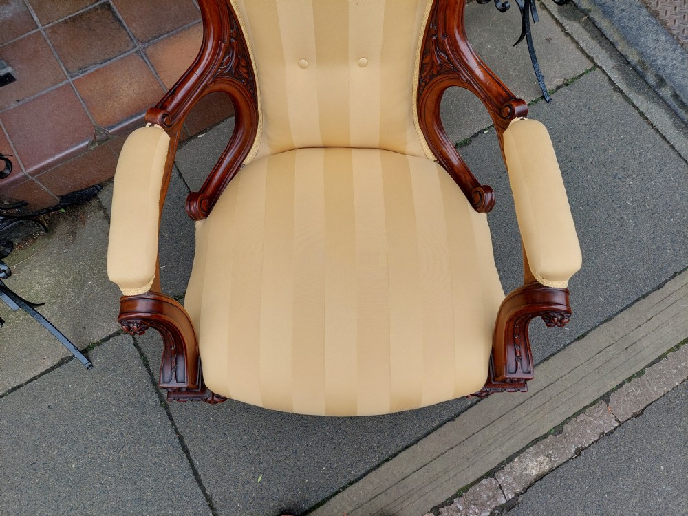 A low Victorian armchair crafted from carved dark walnut with cream striped upholstery and turned legs with brass casters. View VI