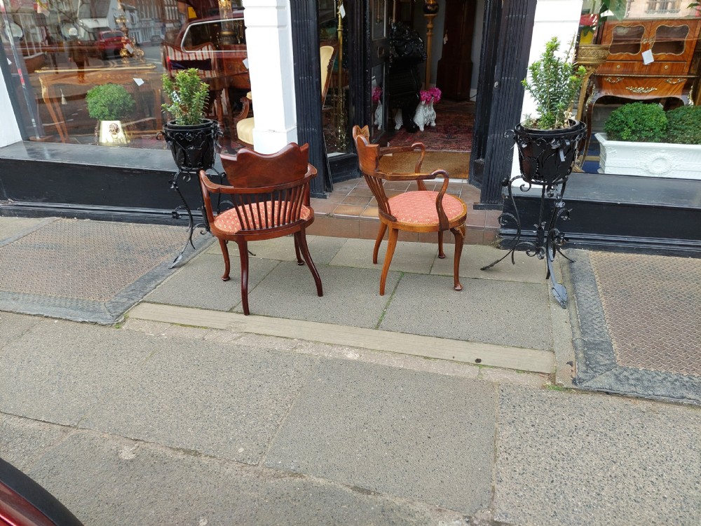 A matched pair of Edwardian mahogany tub armchairs featuring floral marquetry backsplats, thin vertical spindles, cabriole legs, and red patterned fabric seats. View V